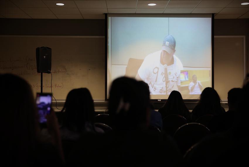 HISD teacher Jonathan Bryant can be seen on a screen in an overflow room during a school board meeting Thursday at HISD headquarters in northwest Houston. (Annie Mulligan for Houston Landing)

