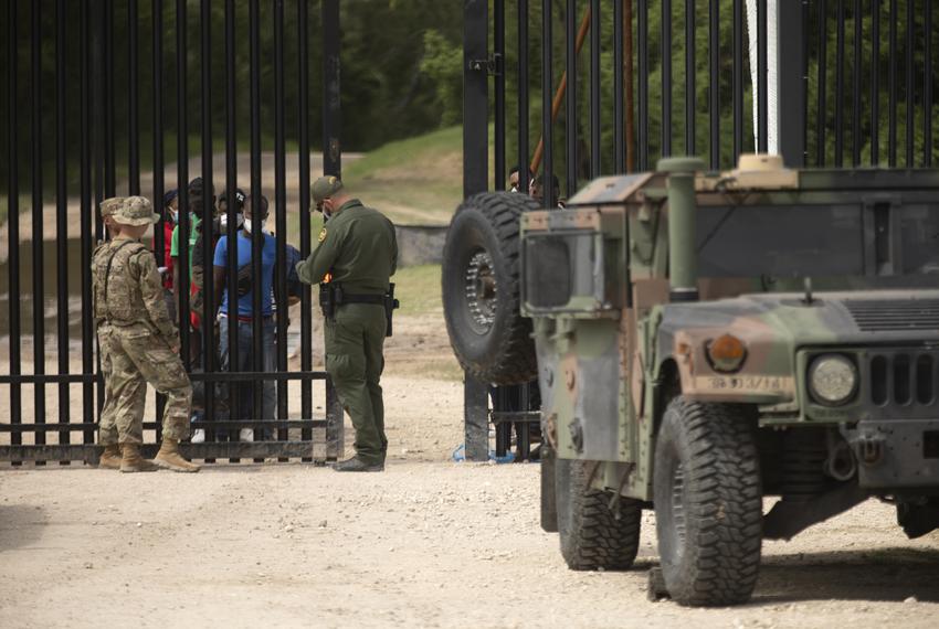 A group migrants waits at a gate near the U.S. and Mexico border in Del Rio on July 22, 2021. The group turned themselves over to the National Guard and Customs and Border Protection officials.